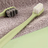 Une brosse à dents vert clair avec des poils blancs repose sur une serviette grise.