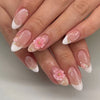 Gros plan d'une main montrant des kits de vernis press-on en forme de fleur d'amande avec des accents rose et blanc.
