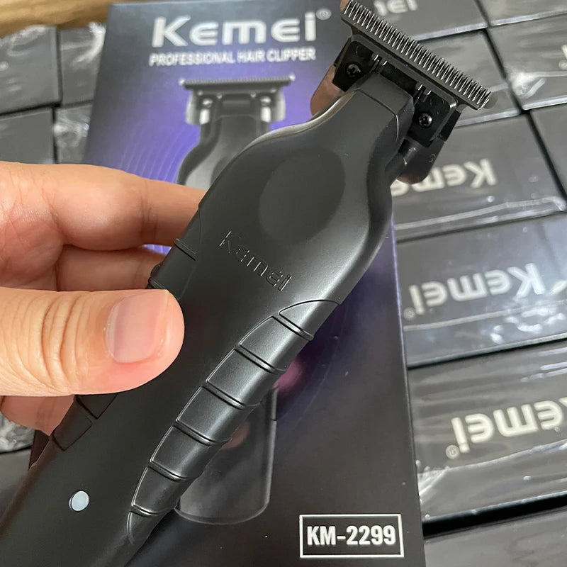 A hand holds a black Kemel professional electric hair clipper trimmer with a protective guard, resting on its packaging.