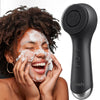A person is using a black facial cleansing brush to apply foam to their face.