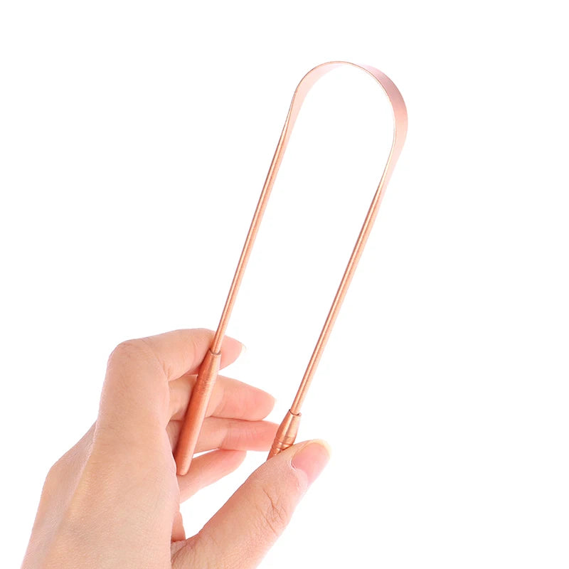 Une main tient un racloir de langue en cuivre, un outil métallique fin et incurvé pour l'hygiène buccale.