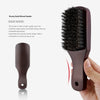 A close-up of a dark brown wooden boar bristle hair and beard brush being held by a hand.
