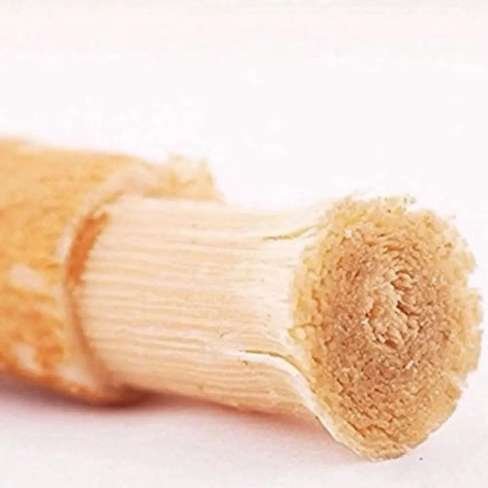 A close-up of a natural miswak toothbrush showing its light brown, fibrous wood handle.