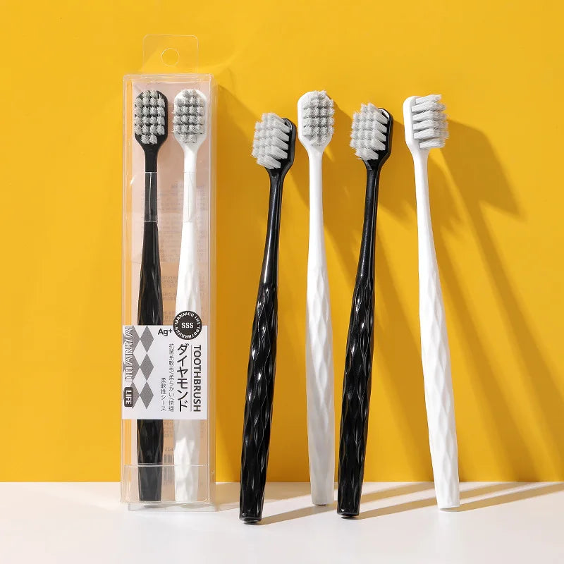 Un set de quatre brosses à dents antibactériennes blanches et noires dans une boîte transparente sur fond jaune.