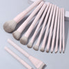 A set of thirteen professional makeup brushes with light pink handles and grey bristles arranged on a white surface.
