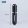 Flacon de parfum cylindrique noir rechargeable avec pompe argentée sur fond gris clair.
