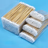 A clear plastic container holds numerous wooden cotton swabs and several packaged bundles of white cotton tips.