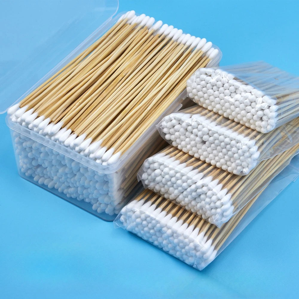 A clear plastic container holds numerous wooden cotton swabs and several packaged bundles of white cotton tips.