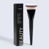 A black packaging box and a black foundation brush with a fluffy white synthetic hair on a light gray background.