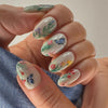 A hand displays 24 press-on nails featuring delicate pink flowers and blue butterflies on a white background.