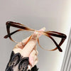 A hand is holding a pair of elegant brown cat eye reading glasses against a light background.