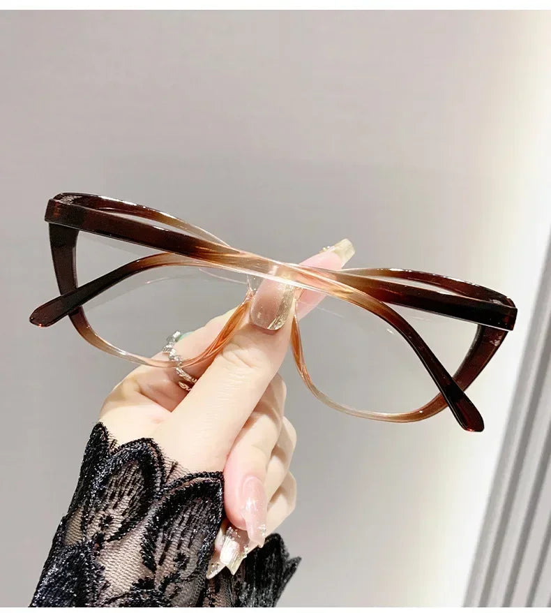 A hand is holding a pair of elegant brown cat eye reading glasses against a light background.