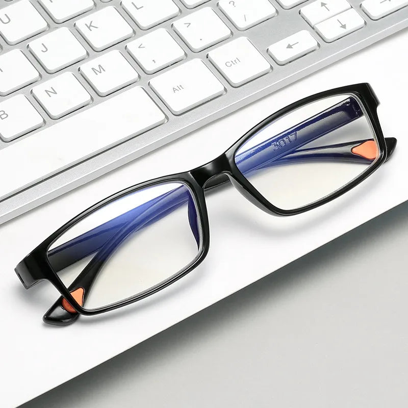 A pair of black-framed reading glasses with blue and orange accents resting on a white keyboard.