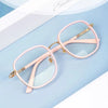 A pair of pink, oversized square reading glasses with gold accents resting on a light blue surface.