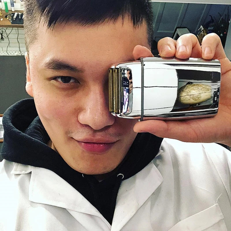 A man holds a silver electric shaver up to his face for a close-up view.