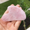 Una mano sostiene un cristal de cuarzo rosa en forma de corazón para masaje facial.