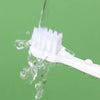 A white cartoon dinosaur toothbrush is being rinsed under running water against a green background.