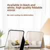 A folding cosmetic mirror in black and white is displayed on a white surface.