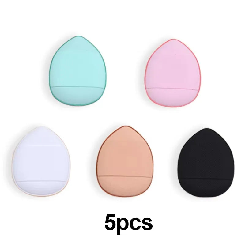 Cinq mini éponges de fondation dans des tons pastel et neutres, dont vert menthe, rose, blanc, pêche et noir.