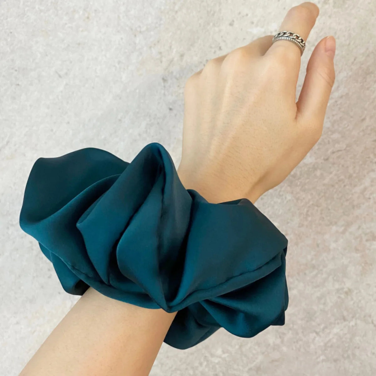 Une main noue un tissu en mousseline satinée couleur bleu sarcelle en nœud ou élastique.