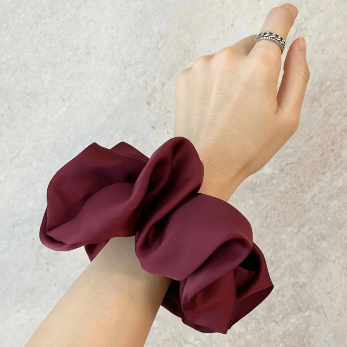 Une main porte un élastique pour cheveux en mousseline de satin bordeaux noué autour du poignet.