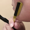 A hand holds a professional stainless steel shaver and beard razor kit, showing the gold and black components against a perso