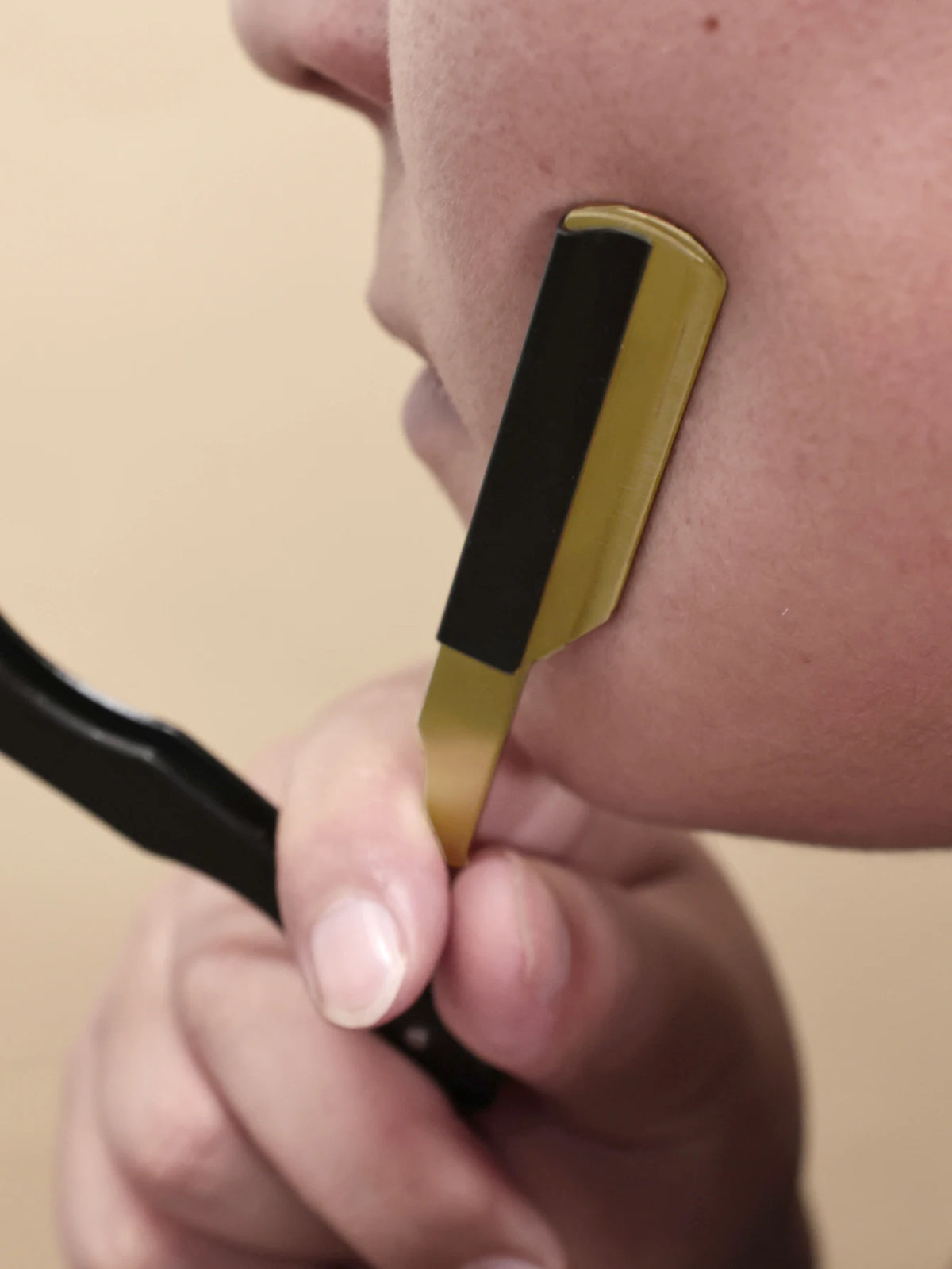 A hand holds a professional stainless steel shaver and beard razor kit, showing the gold and black components against a perso