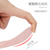 A hand is using a pink silicone facial mask brush with an integrated scraper to apply makeup.