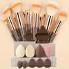 A collection of makeup brushes and sponges in various shades of brown, pink, and orange displayed on a light background.