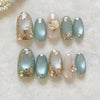 A set of 24 press-on nails featuring a soft pink and mint green gradient with gold floral accents.