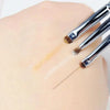 A hand is applying eyeshadow using a precision brush to create a subtle highlight on the skin.