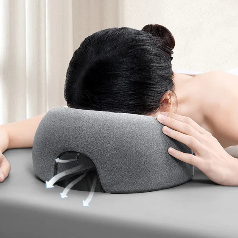A hand is applying pressure to a gray ergonomic memory foam prone pillow for relaxation.