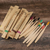 A set of eco-friendly bamboo toothbrushes in various colors and natural wood tones arranged on a wooden surface.