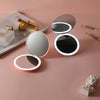 A collection of pink and silver LED makeup mirrors with luminous effects displayed on a light pink surface.