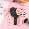 Trois miroirs à cils en forme de cœur portables roses et noirs sont présentés sur un fond rose.