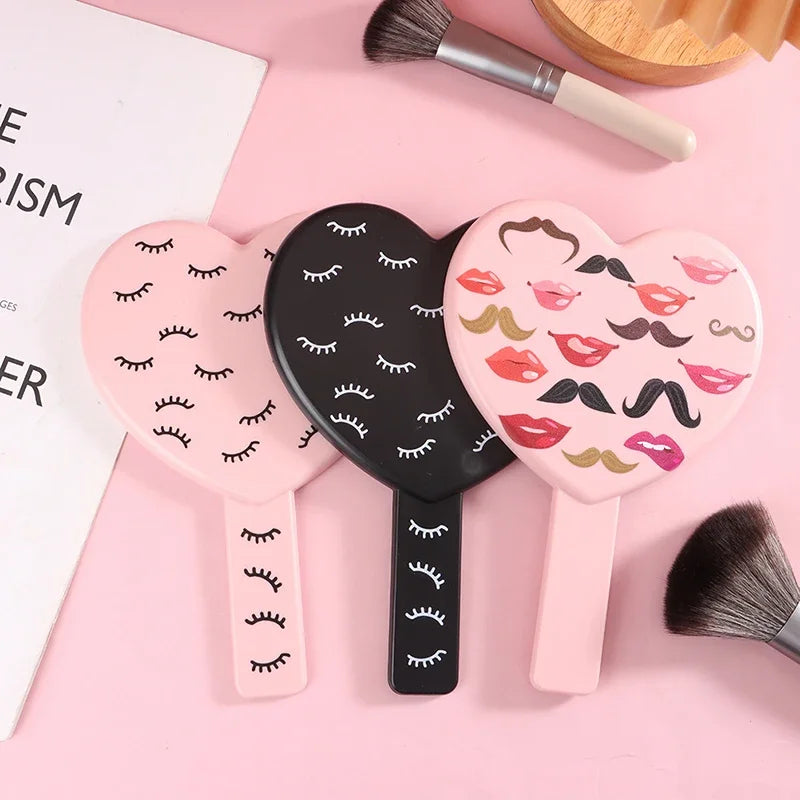 Trois miroirs à cils en forme de cœur portables roses et noirs sont présentés sur un fond rose.