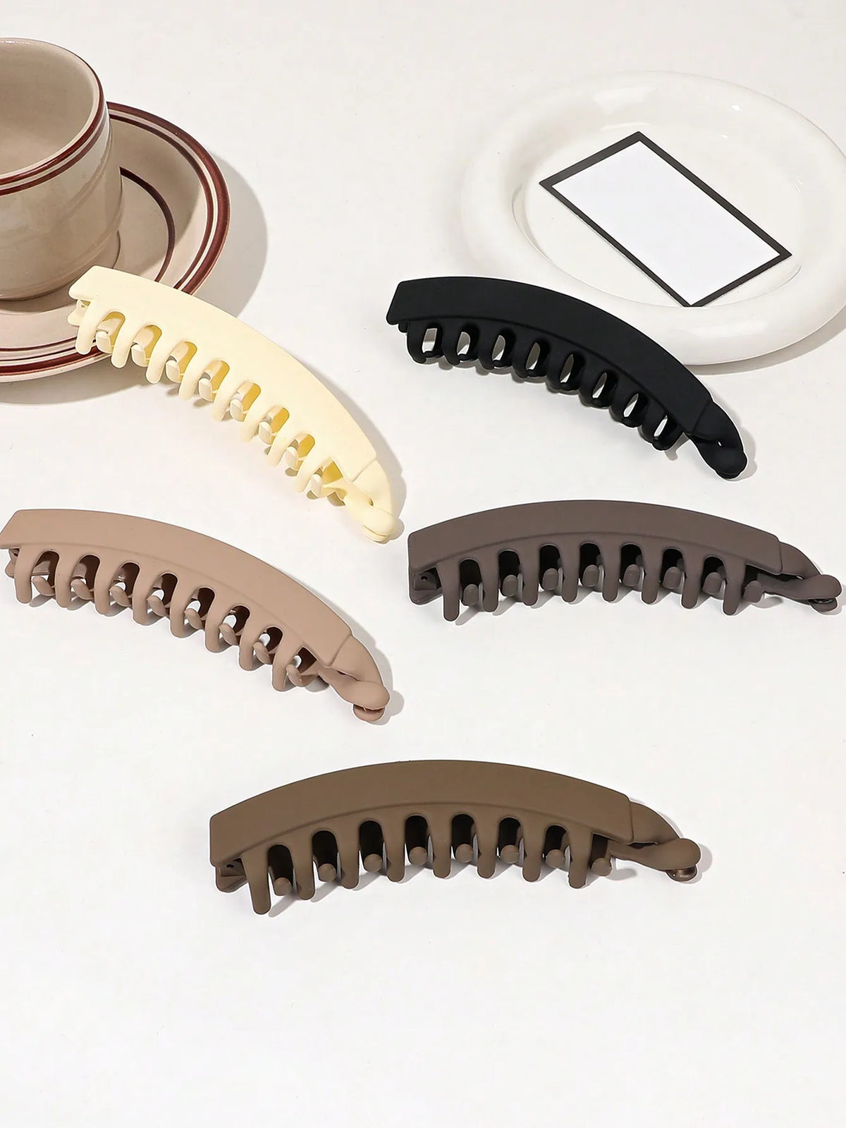 A collection of five banana-shaped hair clips in various shades of beige and brown for strong grip styling.