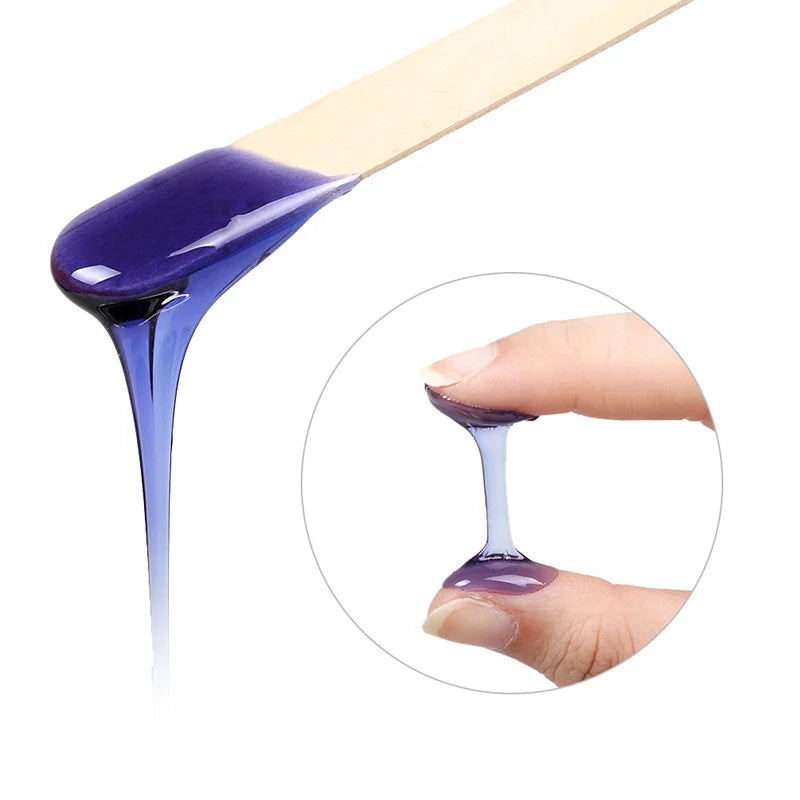 A wooden stick dipped in purple hard wax is shown dripping onto a finger for hair removal.