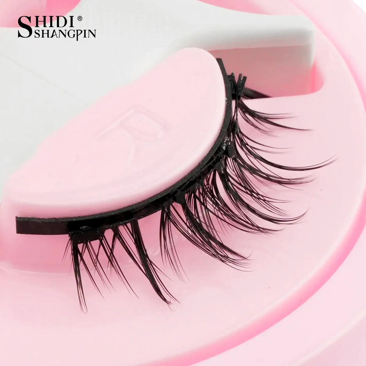 Une bande de faux cils magnétique réutilisable rose est montrée sur un outil en plastique blanc.