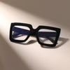 A pair of black square eyeglasses with clear blue lenses resting on a light surface.