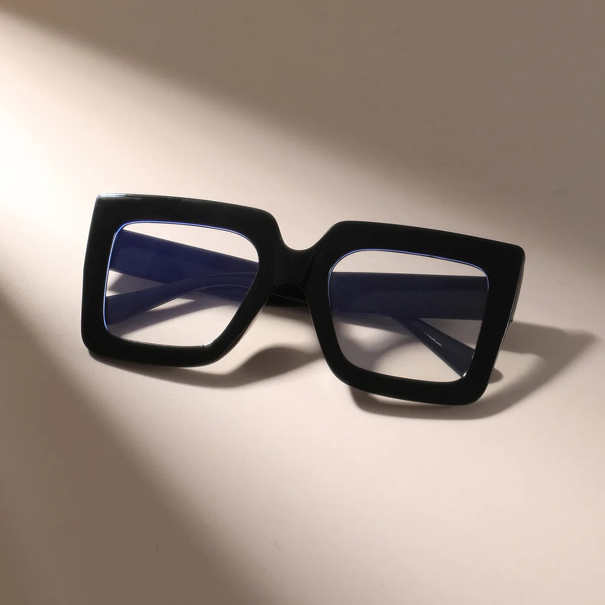 A pair of black square eyeglasses with clear blue lenses resting on a light surface.