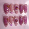 A set of 24 press-on almond nails featuring various shades of purple and delicate 3D floral designs.
