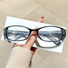 A pair of black anti-blue light reading glasses resting on a white card, held by a person's hand.