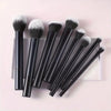 A set of nine black makeup brushes with fluffy and dense bristles displayed on a light pink surface.