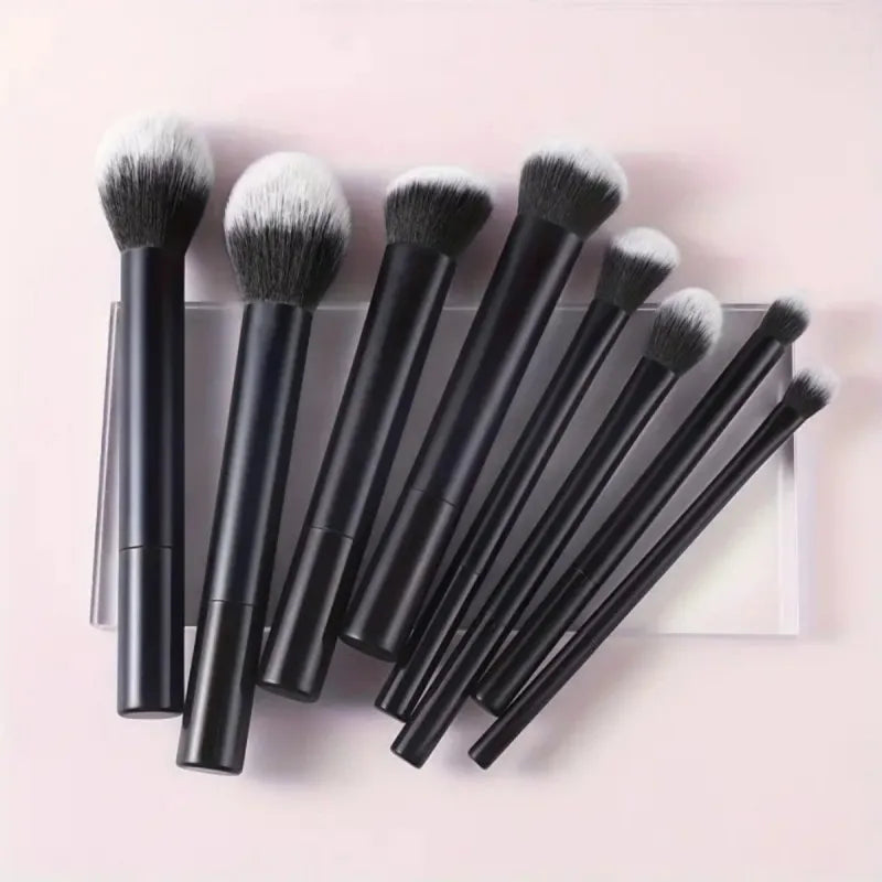 A set of nine black makeup brushes with fluffy and dense bristles displayed on a light pink surface.