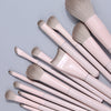 A collection of thirteen professional makeup brushes with light pink handles and natural hair bristles.