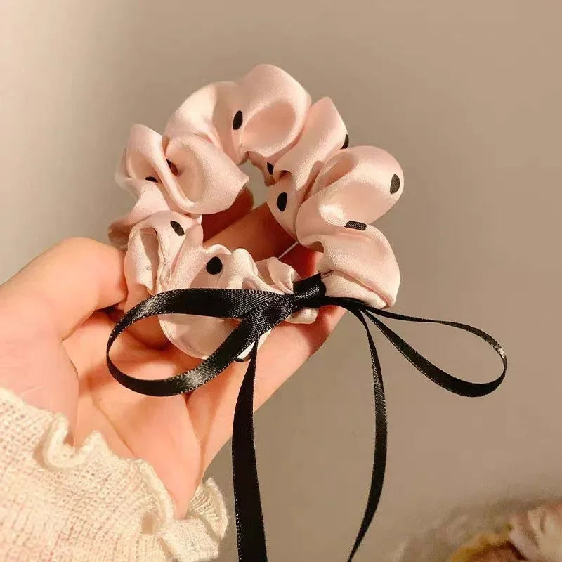 Scrunchies en satin roses à pois noirs, attachés avec un ruban noir