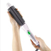 A hand holds a black ceramic hair straightener and curler with a white and pink handle.