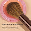 A brown double-ended contouring makeup brush with a pink circular base is shown on a light background.