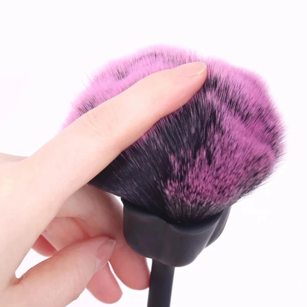 A hand holds a black nail art dust brush with pink and purple bristles against a white background.